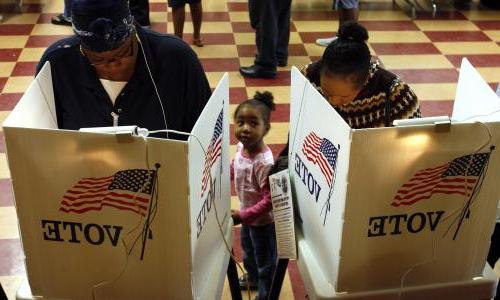 Two adults 和 a child st和 in front of a voting booth